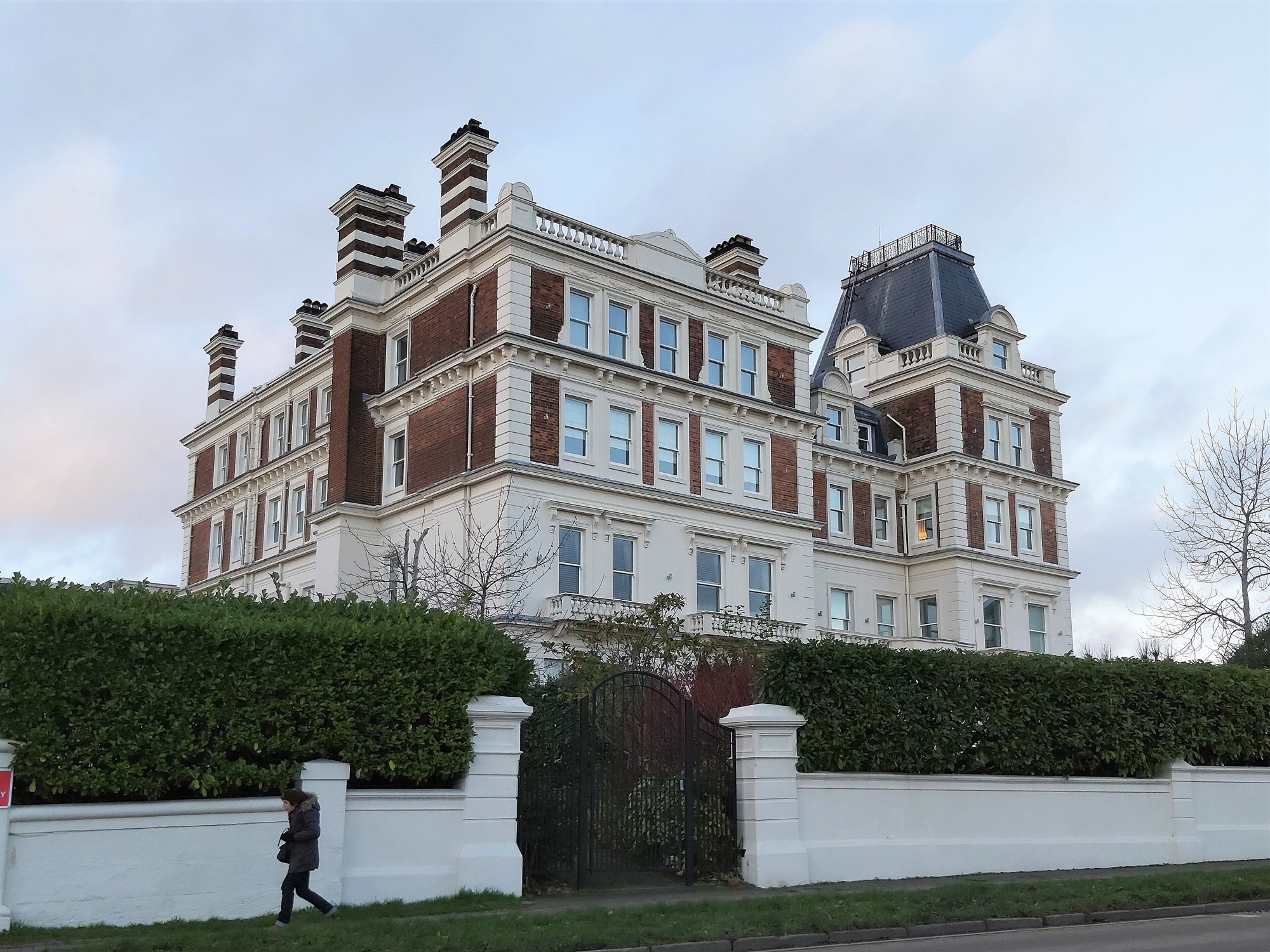A white and red brick period building converted into residential flats behind a hedge